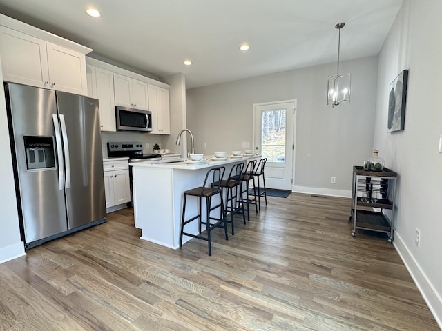 kitchen featuring hardwood / wood-style flooring, stainless steel appliances, an island with sink, and white cabinets