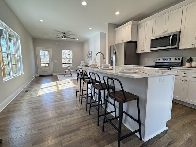 kitchen featuring a center island with sink, white cabinets, stainless steel appliances, and a breakfast bar area