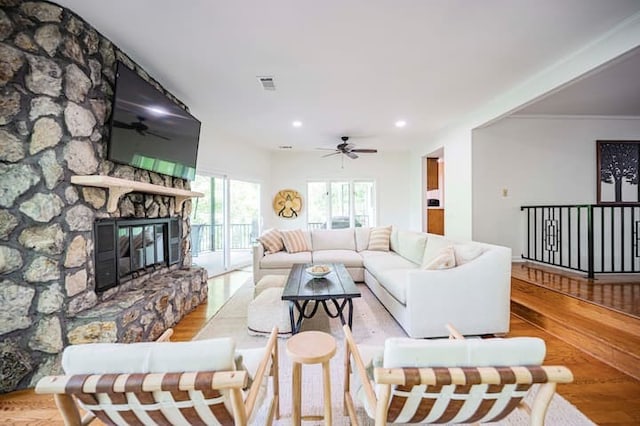 living room with ceiling fan, a stone fireplace, and light hardwood / wood-style floors