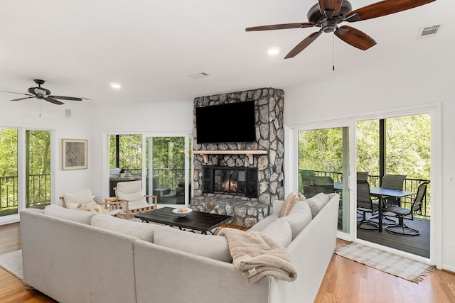 living room featuring a healthy amount of sunlight, ceiling fan, a stone fireplace, and light hardwood / wood-style floors