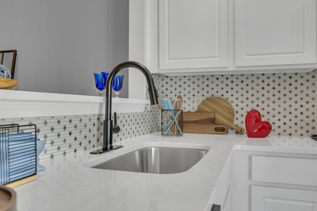 interior details featuring light stone counters, white cabinetry, sink, and tasteful backsplash