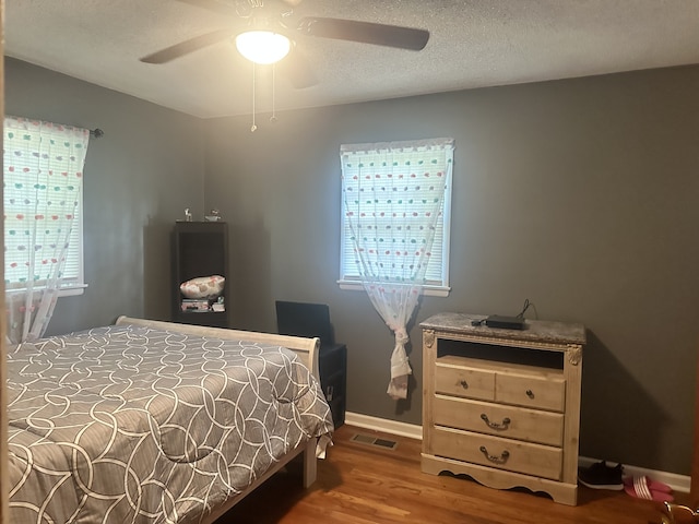 bedroom with multiple windows, hardwood / wood-style floors, a textured ceiling, and ceiling fan