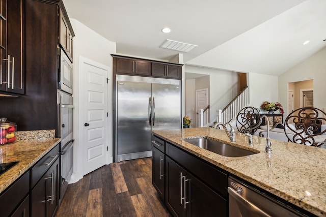 kitchen featuring sink, dark brown cabinets, built in appliances, light stone counters, and dark wood-type flooring