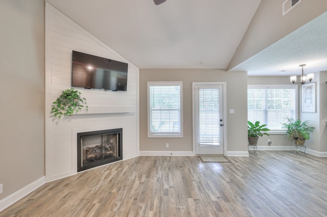 unfurnished living room with an inviting chandelier, vaulted ceiling, a fireplace, hardwood / wood-style flooring, and a textured ceiling