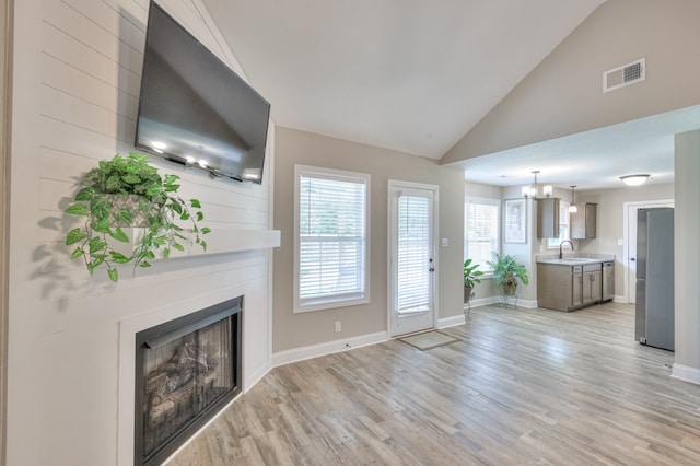 unfurnished living room with high vaulted ceiling, sink, a chandelier, and light hardwood / wood-style flooring