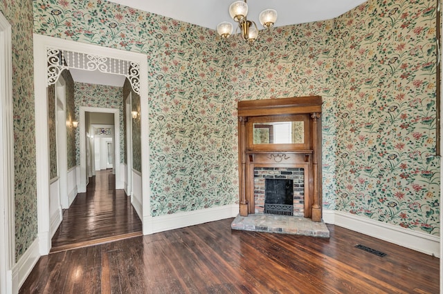 unfurnished living room with a brick fireplace, a notable chandelier, and dark hardwood / wood-style flooring