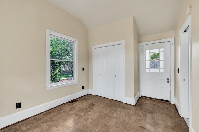 foyer with a healthy amount of sunlight, vaulted ceiling, and light colored carpet