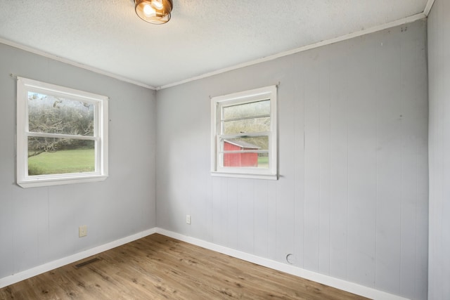 spare room with light hardwood / wood-style flooring, wooden walls, and a textured ceiling