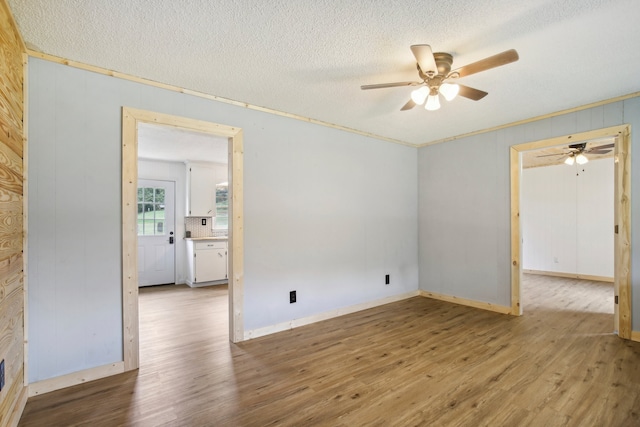 unfurnished room with wooden walls, ceiling fan, light hardwood / wood-style floors, and a textured ceiling