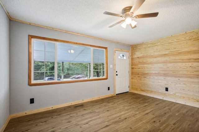 spare room with a textured ceiling, wood-type flooring, wooden walls, and ceiling fan