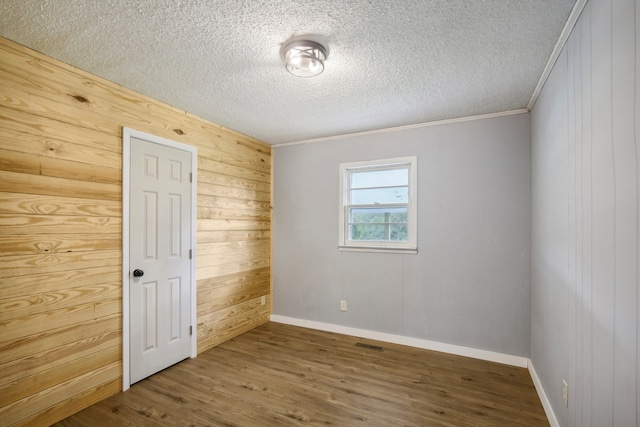 unfurnished room with wooden walls, crown molding, wood-type flooring, and a textured ceiling