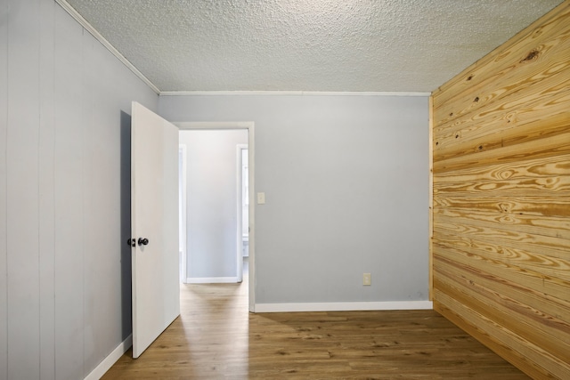 empty room with wood walls, ornamental molding, hardwood / wood-style flooring, and a textured ceiling