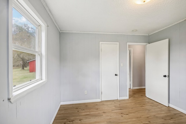 spare room featuring light hardwood / wood-style floors, crown molding, a wealth of natural light, and a textured ceiling