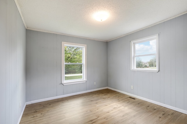 empty room with ornamental molding, wooden walls, light hardwood / wood-style floors, and a textured ceiling