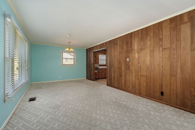 carpeted empty room with wood walls, crown molding, and a chandelier