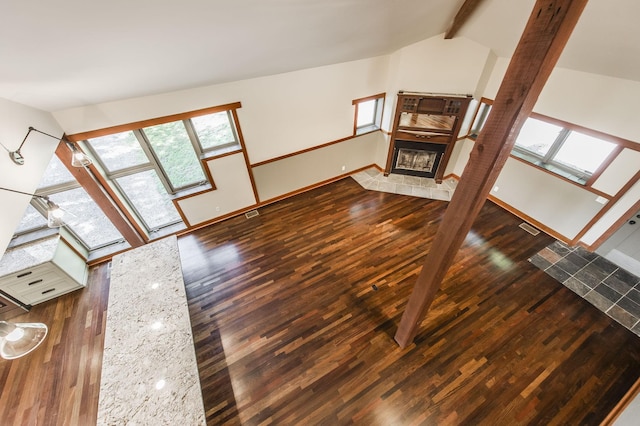 unfurnished living room with visible vents, wood finished floors, a tile fireplace, baseboards, and vaulted ceiling with beams