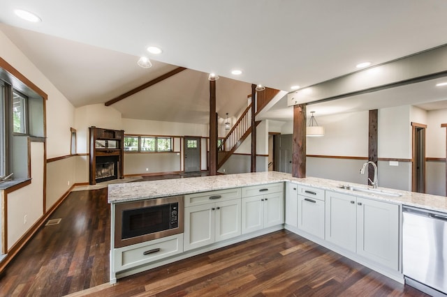 kitchen with a sink, dishwasher, built in microwave, vaulted ceiling, and dark wood-style floors