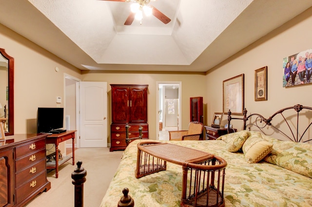 bedroom with ceiling fan, a raised ceiling, light carpet, and ensuite bathroom