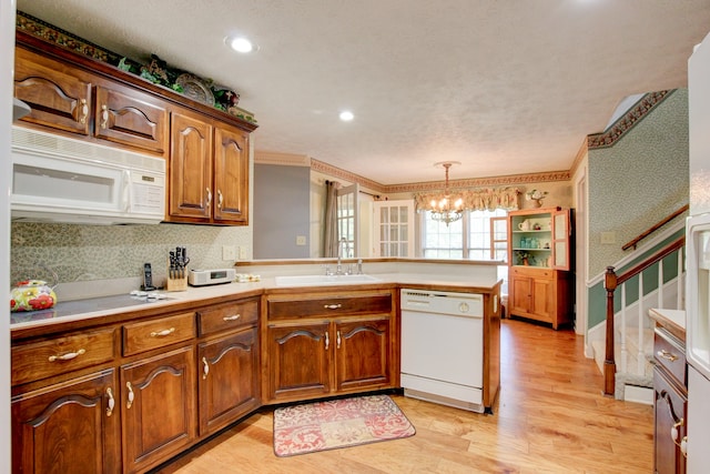 kitchen featuring light wood-type flooring, pendant lighting, white appliances, a notable chandelier, and sink