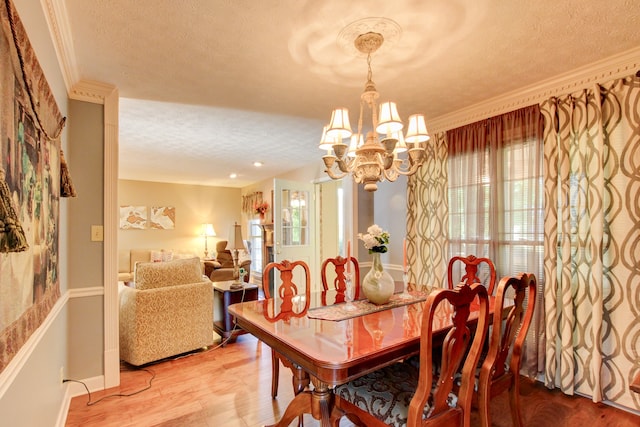 dining area featuring wood-type flooring, crown molding, a notable chandelier, and a textured ceiling