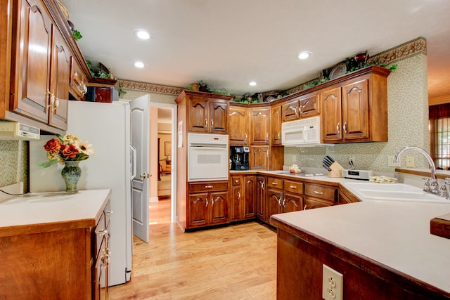 kitchen with backsplash, white appliances, sink, and light hardwood / wood-style flooring