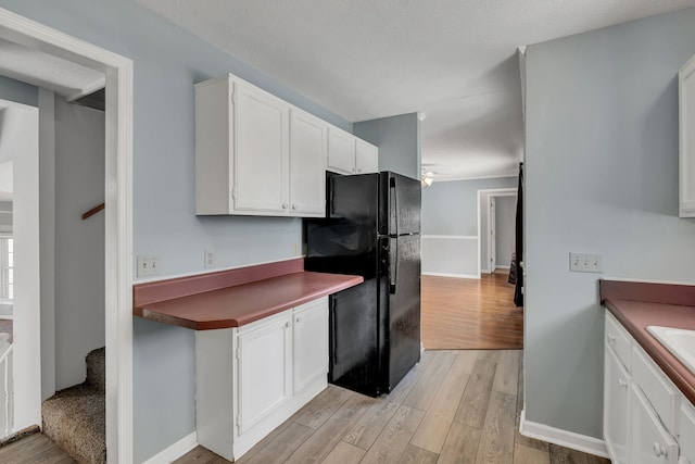 kitchen with white cabinets, a textured ceiling, light wood-type flooring, and black refrigerator