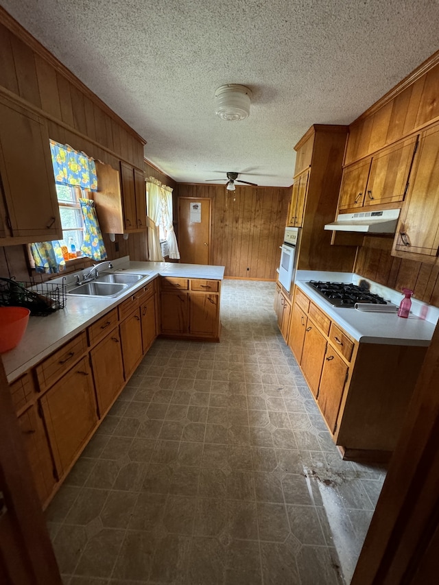 kitchen featuring wood walls, ceiling fan, white appliances, sink, and kitchen peninsula