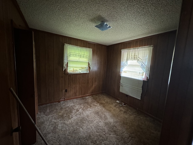 empty room with a textured ceiling, wood walls, and dark colored carpet