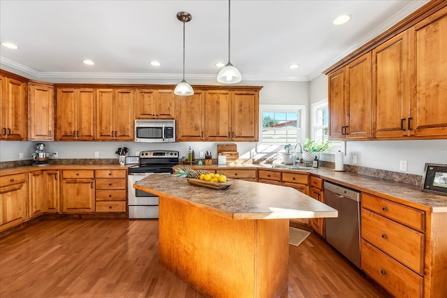 kitchen featuring wood-type flooring, hanging light fixtures, appliances with stainless steel finishes, ornamental molding, and a center island