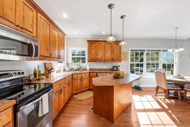 kitchen featuring pendant lighting, light hardwood / wood-style flooring, appliances with stainless steel finishes, a center island, and crown molding