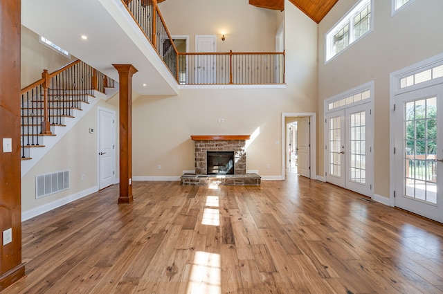 unfurnished living room featuring high vaulted ceiling, a stone fireplace, french doors, and wood-type flooring