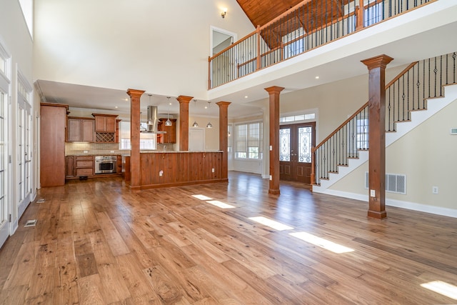 unfurnished living room with french doors, high vaulted ceiling, decorative columns, and light wood-type flooring