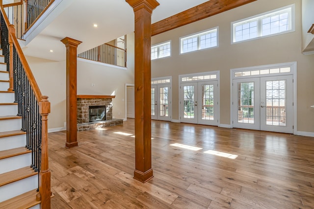 unfurnished living room with french doors, a stone fireplace, decorative columns, and light hardwood / wood-style floors