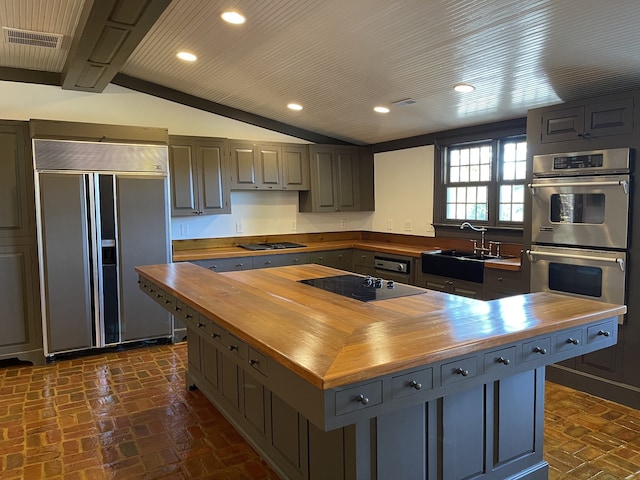 kitchen featuring black electric cooktop, lofted ceiling, paneled built in refrigerator, double oven, and butcher block counters