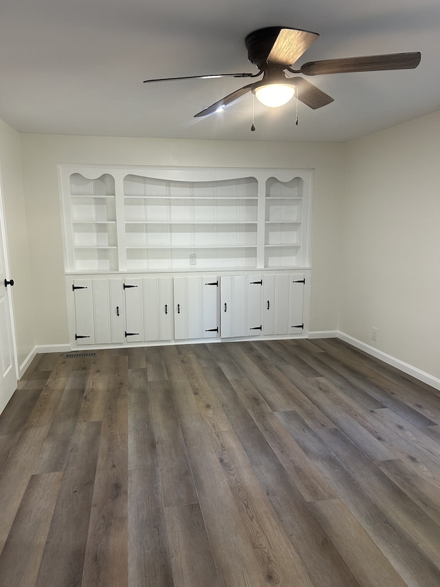 unfurnished room featuring dark hardwood / wood-style floors, built in shelves, and ceiling fan