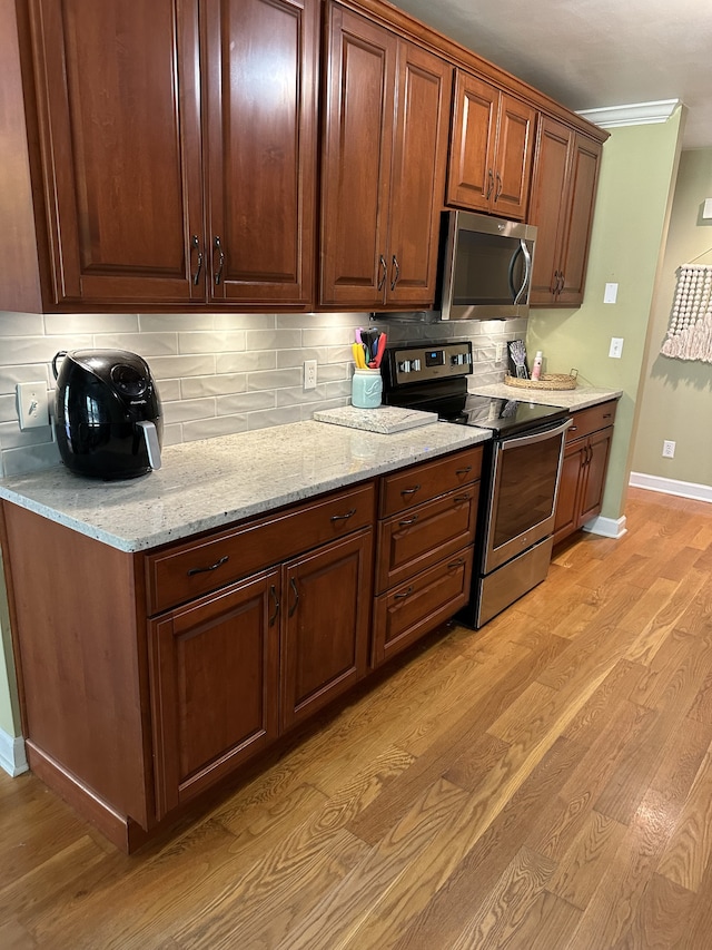 kitchen featuring light wood-type flooring, light stone countertops, stainless steel appliances, and backsplash