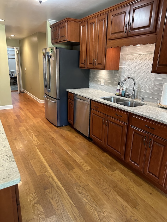 kitchen with light hardwood / wood-style flooring, sink, light stone countertops, backsplash, and appliances with stainless steel finishes