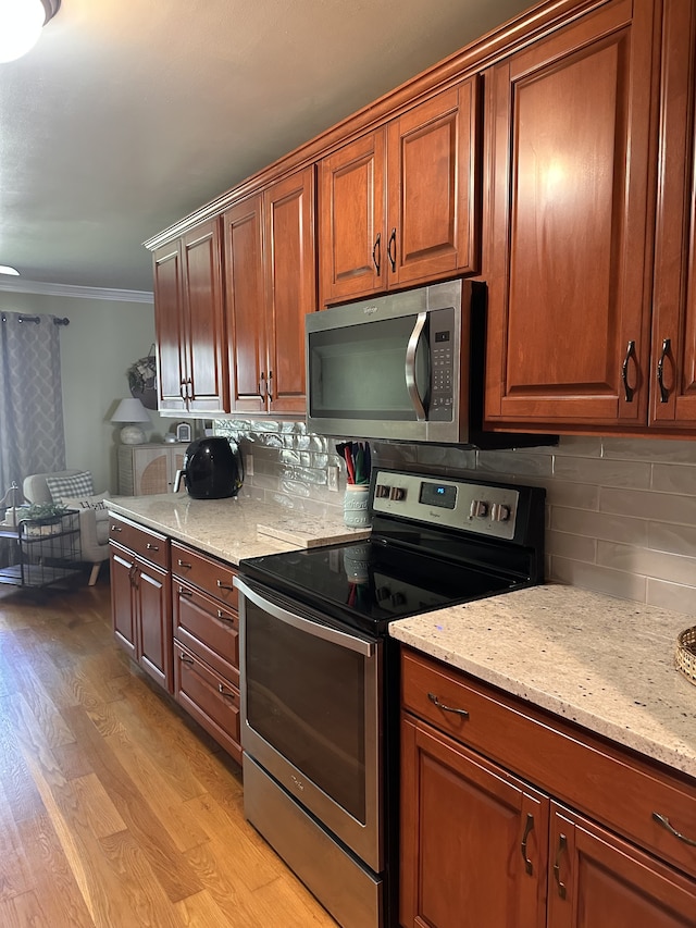 kitchen with light stone counters, tasteful backsplash, stainless steel appliances, light wood-type flooring, and crown molding