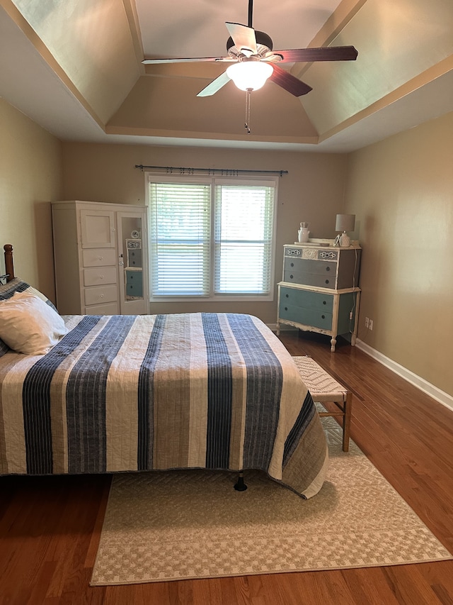 bedroom featuring ceiling fan, a raised ceiling, and dark wood-type flooring