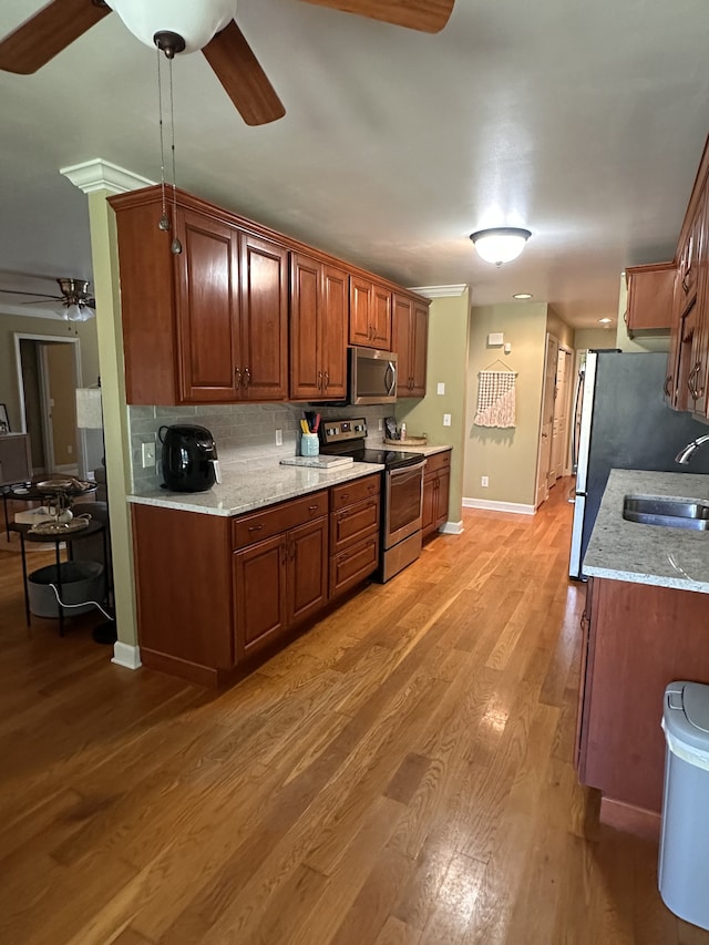 kitchen featuring stainless steel appliances, sink, light wood-type flooring, and light stone counters