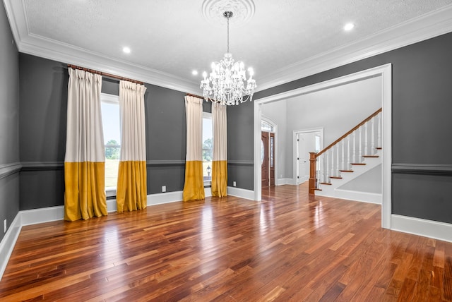 empty room with ornamental molding, hardwood / wood-style floors, a notable chandelier, and a textured ceiling