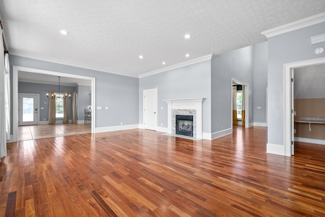 unfurnished living room featuring a stone fireplace, hardwood / wood-style flooring, an inviting chandelier, ornamental molding, and a textured ceiling