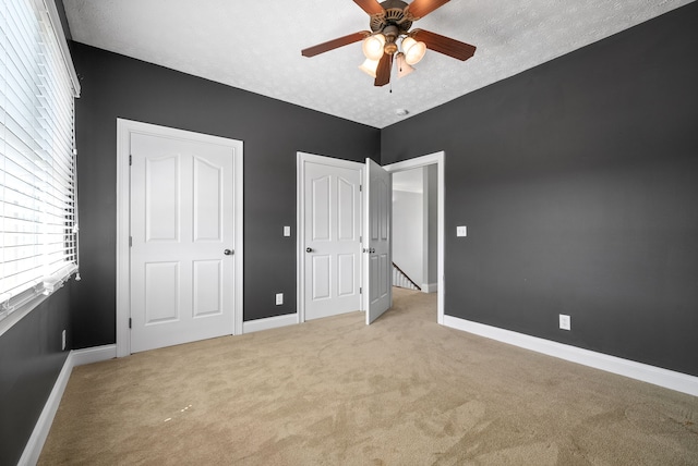 unfurnished bedroom featuring light colored carpet, a textured ceiling, and ceiling fan