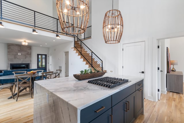 kitchen featuring light hardwood / wood-style floors, a tile fireplace, a kitchen island, decorative light fixtures, and stainless steel gas stovetop