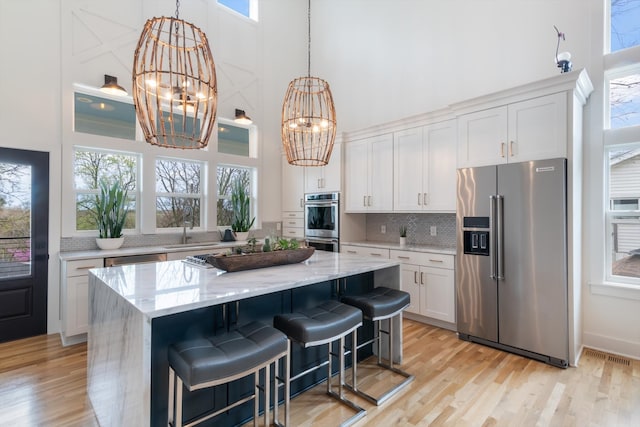 kitchen with appliances with stainless steel finishes, a healthy amount of sunlight, a high ceiling, and white cabinets