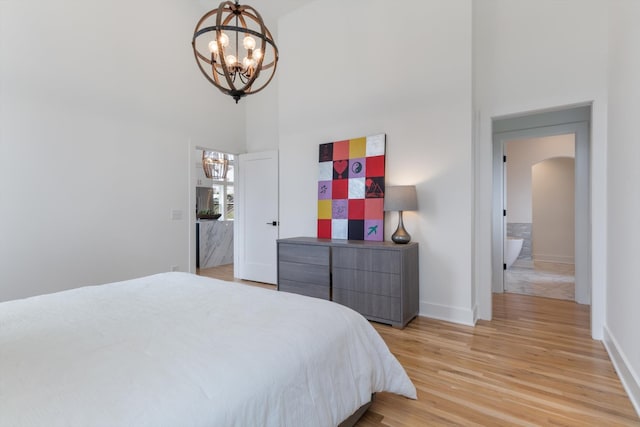 bedroom featuring a notable chandelier, a towering ceiling, and light hardwood / wood-style flooring