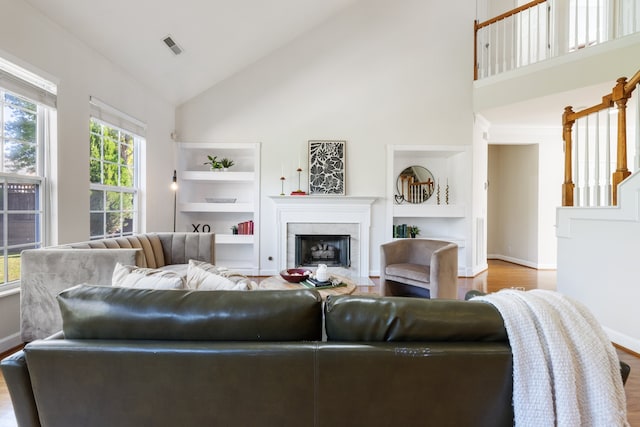 living room with high vaulted ceiling, built in shelves, and light hardwood / wood-style floors