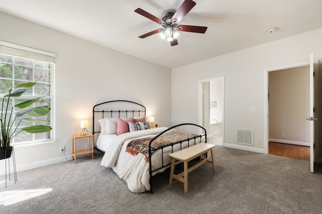 carpeted bedroom featuring ceiling fan, ensuite bathroom, and multiple windows