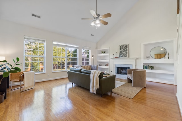 living room featuring built in shelves, light hardwood / wood-style floors, high vaulted ceiling, and ceiling fan