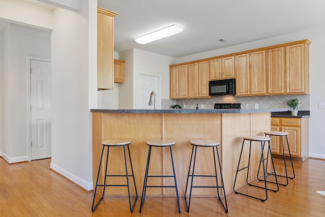 kitchen featuring kitchen peninsula, tasteful backsplash, light brown cabinetry, a breakfast bar area, and light wood-type flooring